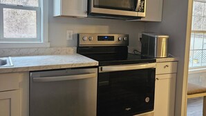 A compact kitchen with white cabinets, a stainless steel dishwasher, an oven, a microwave, and a coffee maker.