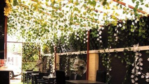 An outdoor seating area with tables and chairs, surrounded by greenery and a wall with climbing plants.