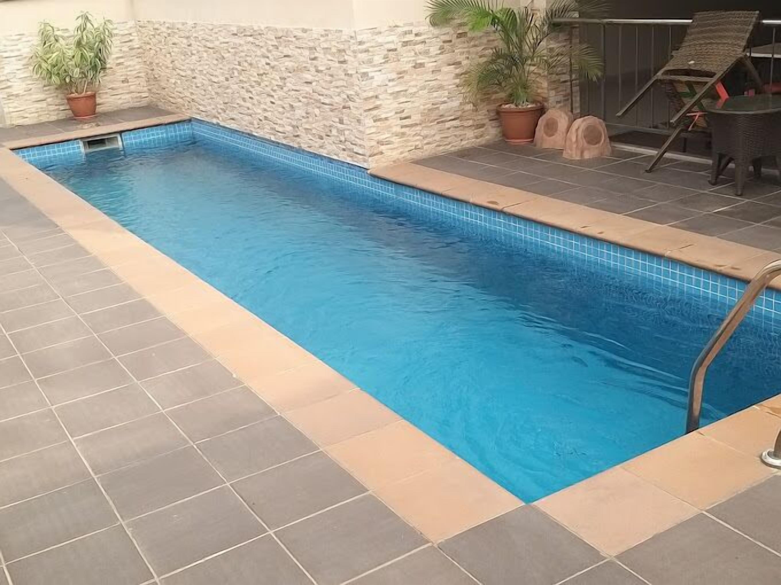 A rectangular indoor pool with blue tiles, surrounded by stone walls and potted plants.