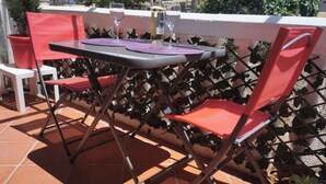 En terrasse med et bord og stole, en flaske vin og en kurv med planter.