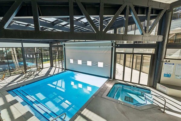 Una piscina interior con paredes de vidrio transparente, estructura de techo y una pequeña piscina contigua.