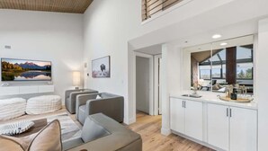 A modern living room with a sofa, a flat-screen TV, and a dining area with a kitchen counter. - SilverKing Mountainside Penthouse - Sleeps 12 (Park City)