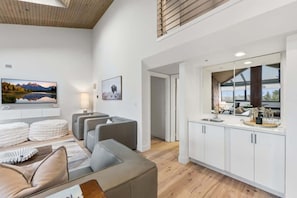 A modern living room with a sofa, a flat-screen TV, and a dining area with a kitchen counter.