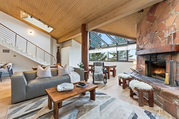A spacious living area with a stone fireplace, a wooden ceiling, and a staircase.