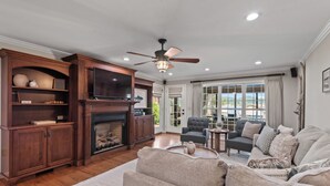A spacious living room with a fireplace, a large sofa, a television, and a ceiling fan.