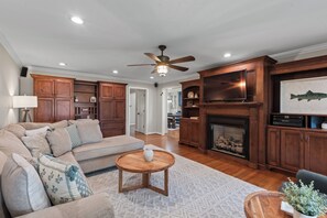 Ein geräumiges Wohnzimmer mit einem Ecksofa, Holzausbau, einem Kamin und einem Deckenventilator.