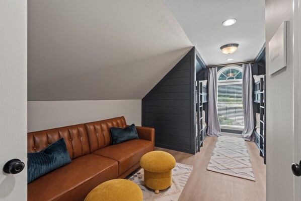 A modern living room with a brown leather sofa, two mustard-colored ottomans, and a patterned rug.