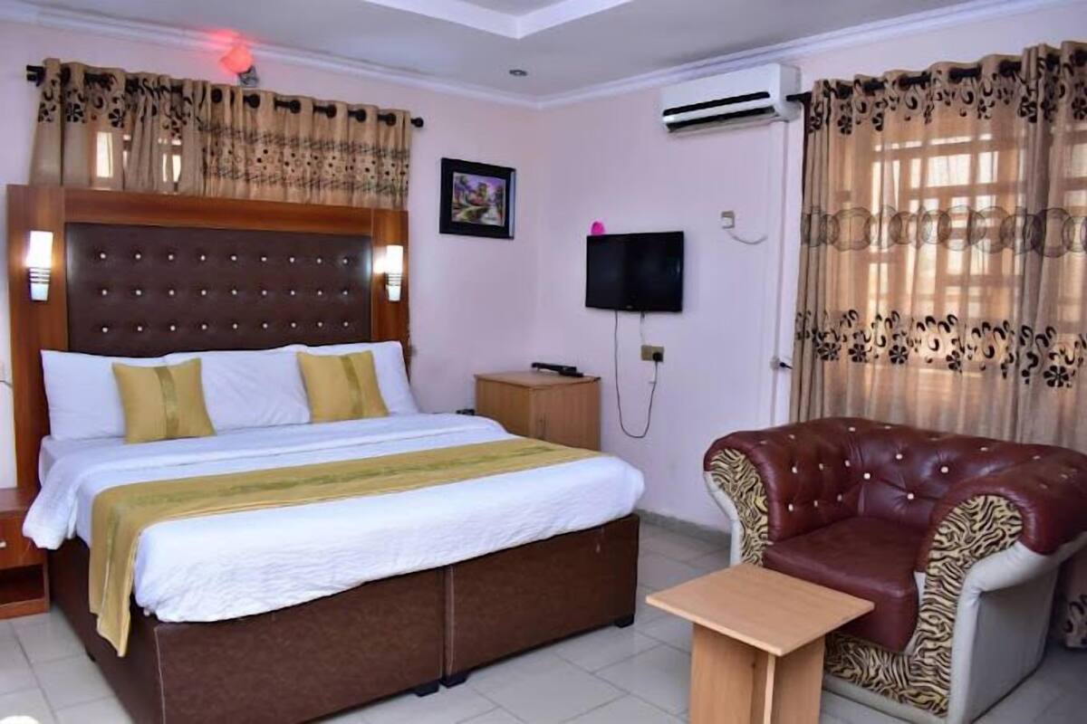 Une chambre d’hôtel avec un grand lit, un fauteuil en cuir, une petite table, un téléviseur et un appareil de climatisation.