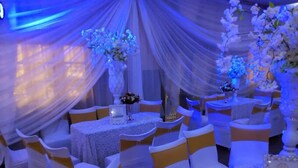 Une salle de banquet avec des tables rondes, des chaises blanches ornées de rubans jaunes et un éclairage d’ambiance bleuté.
