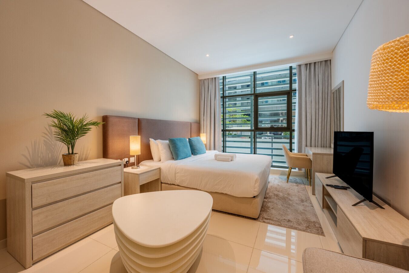 Une chambre d’hôtel moderne équipée d’un lit, de tables de chevet, d’une télévision, d’un bureau et d’une grande fenêtre.