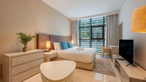 Una camera d'albergo moderna con un letto, comodini, una TV, una scrivania e un'ampia finestra.