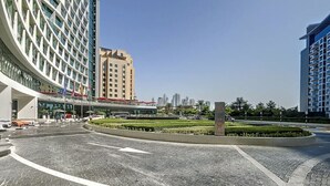 Un moderno incrocio cittadino con un'area verde, edifici alti e cielo sereno.