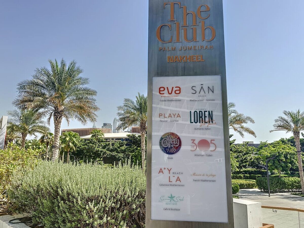 A sign for The Club Palm Jumeirah Nakheel with various restaurant logos.