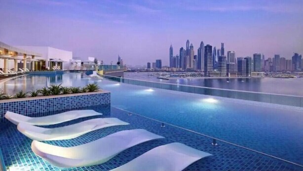 Una piscina a sfioro moderna con vista sullo skyline cittadino, un edificio bianco con tetto curvo e cielo sereno.