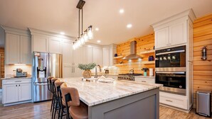 Una cocina moderna con armarios blancos, una isla grande con taburetes de bar, electrodomésticos de acero inoxidable y detalles de madera.