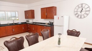 Een moderne keuken met houten kastjes, een witte koelkast, een klok en een eettafel met stoelen.