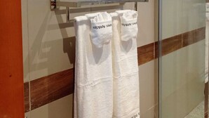 Een badkamer met een glazen douchedeur, een handdoekrek met witte handdoeken, en een lijst met een kunstwerk erboven.