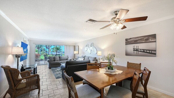 A modern living room with a dining area, a ceiling fan, and a view of the outdoors.