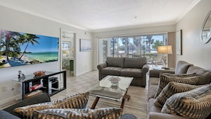 A spacious living room with a large flat-screen TV, comfortable seating, and a view of the outdoors through large windows. - Siesta Key 2/2 Ground Floor  Gulf Views Steps to  Beach (Siesta Key)