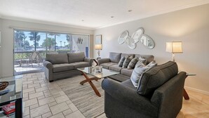 A modern living room with two sofas, a glass coffee table, and a large window with a view of palm trees. - Siesta Key 2/2 Ground Floor  Gulf Views Steps to  Beach (Siesta Key)