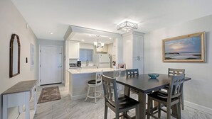 A modern kitchen with white cabinets, a central island, and a dining area with a dark wooden table and chairs.