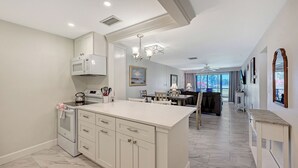A modern kitchen with a central island, white cabinetry, and a dining area with a view.