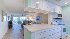 A modern kitchen with white cabinets, a large island, and a dining area with chairs. - Panoramic Gulf Views 2 Bed 2 Bath at Siesta Key Beach Steps to Gulf (Siesta Key)