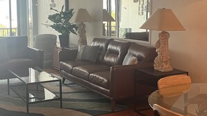 Una sala moderna con un sofá de cuero, dos lámparas, una mesa de centro de vidrio y un ventanal con vistas.