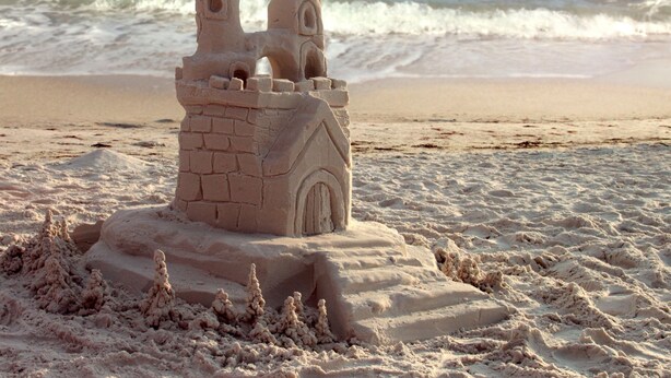 Un castillo de arena en la playa, con vista despejada al océano y tierra a lo lejos.