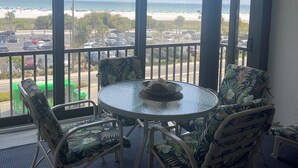 Un balcón con mesa y sillas, vistas a una playa y un estacionamiento.