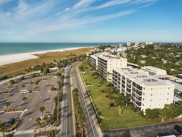 Un hotel de varios pisos con estacionamiento, vista a la playa y una carretera que conduce a la playa.