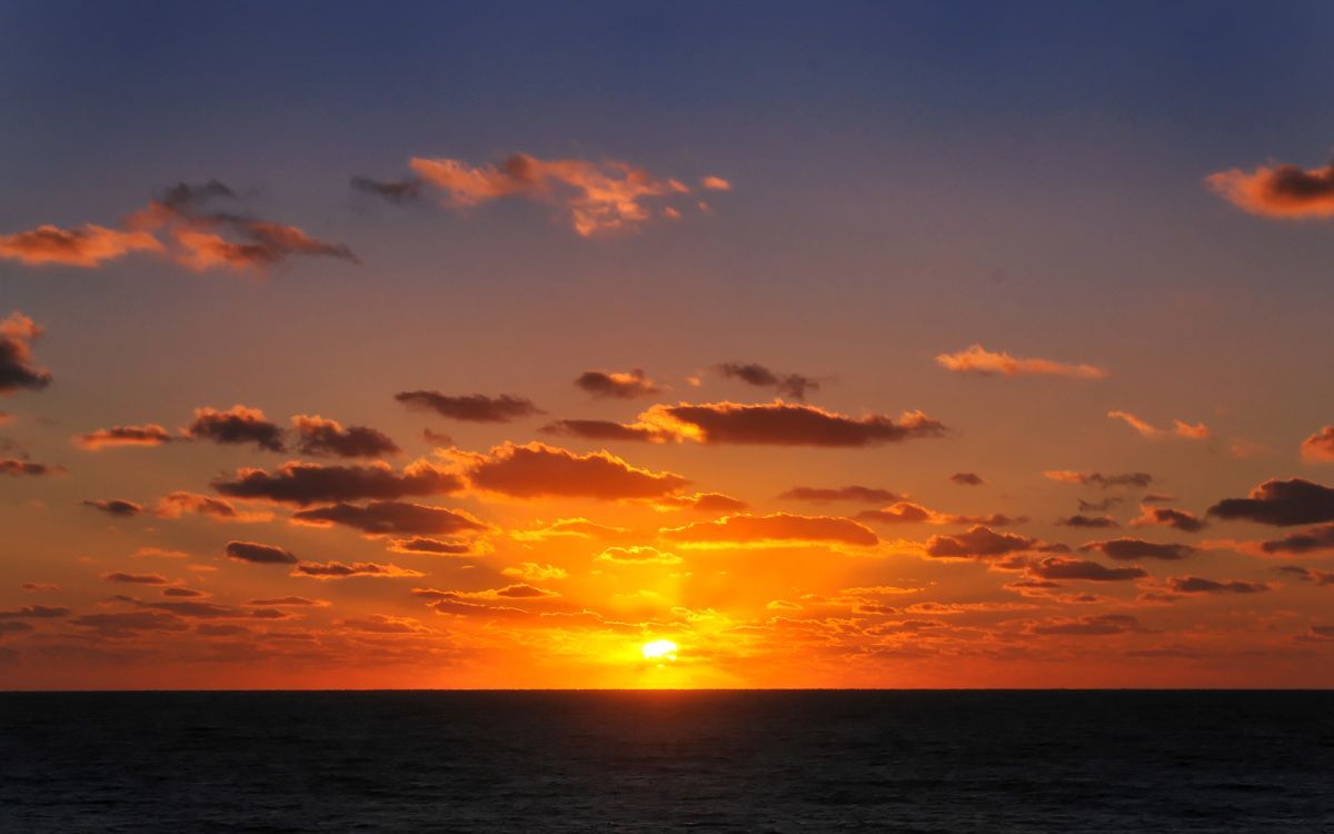 Atardecer sobre el océano con nubes en el cielo.