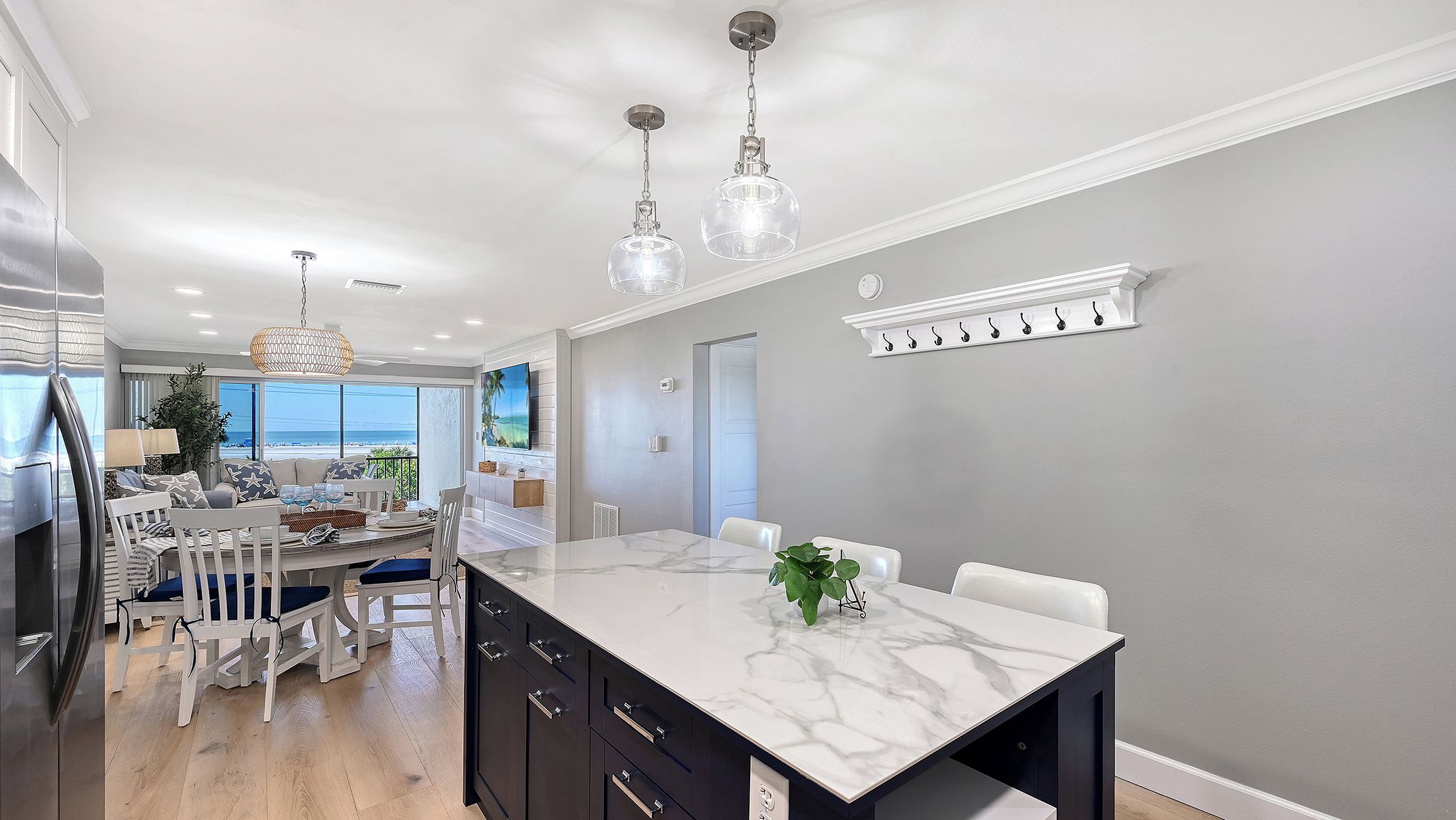 A modern kitchen with a marble countertop, a dining area with a large table, and a view of the ocean.