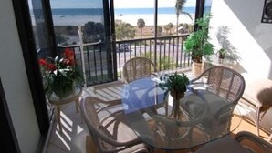 A balcony with a view of the beach, wicker furniture, and potted plants.