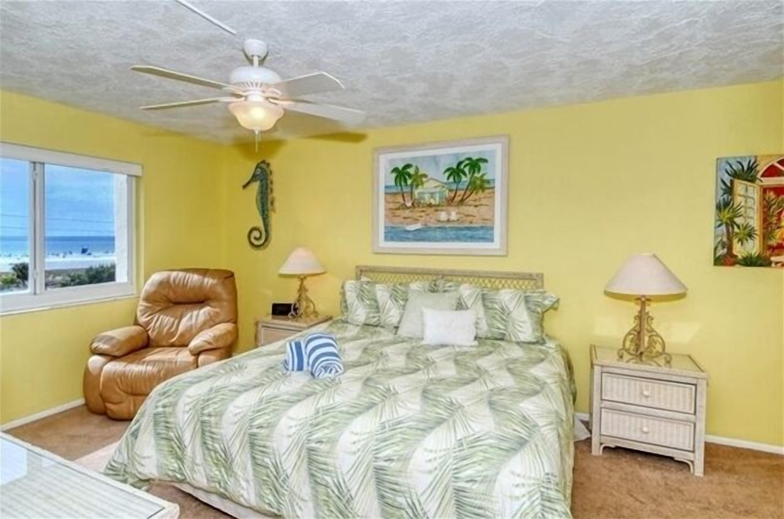 A bedroom with a bed, a chair, a ceiling fan, and a nightstand with lamps.