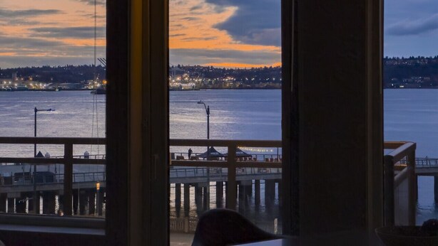 Blick aus einem Fenster auf einen Hafen mit einem Steg und weiter entfernten Stadtlichtern.
