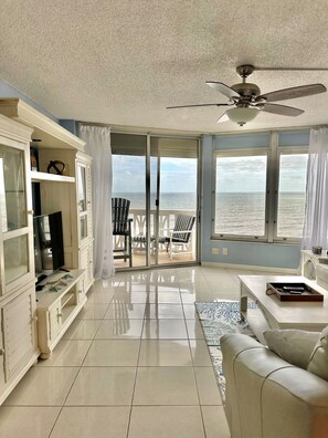 A spacious living room with a large sliding glass door leading to a balcony with a view of the sea.