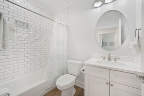 A modern bathroom with white subway tiles, a white toilet, a bathtub, and a vanity with a mirror. - Modern One Bedroom Lockout (Panama City Beach)