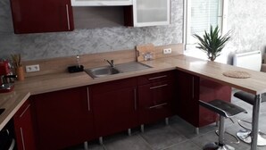 Une cuisine moderne avec des meubles de couleur rouge foncé, un plan de travail en bois clair, un évier en acier inoxydable et un tabouret de bar.