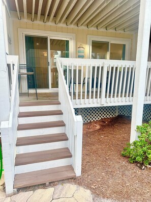 A wooden staircase leading to a porch with a white railing, a bench, and a welcome sign.