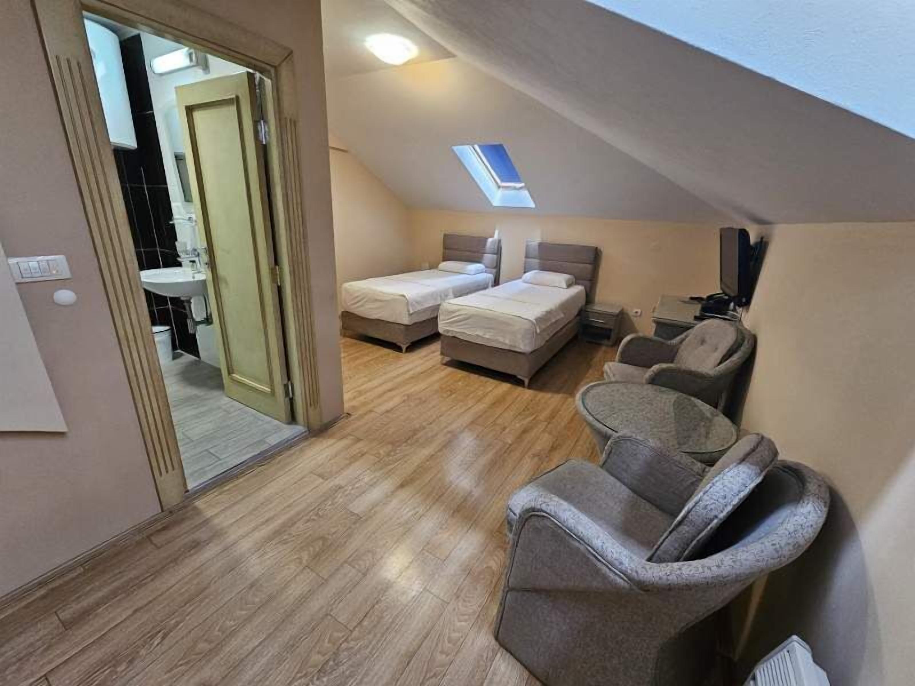 A compact bedroom with two beds, a small desk, and a chair.