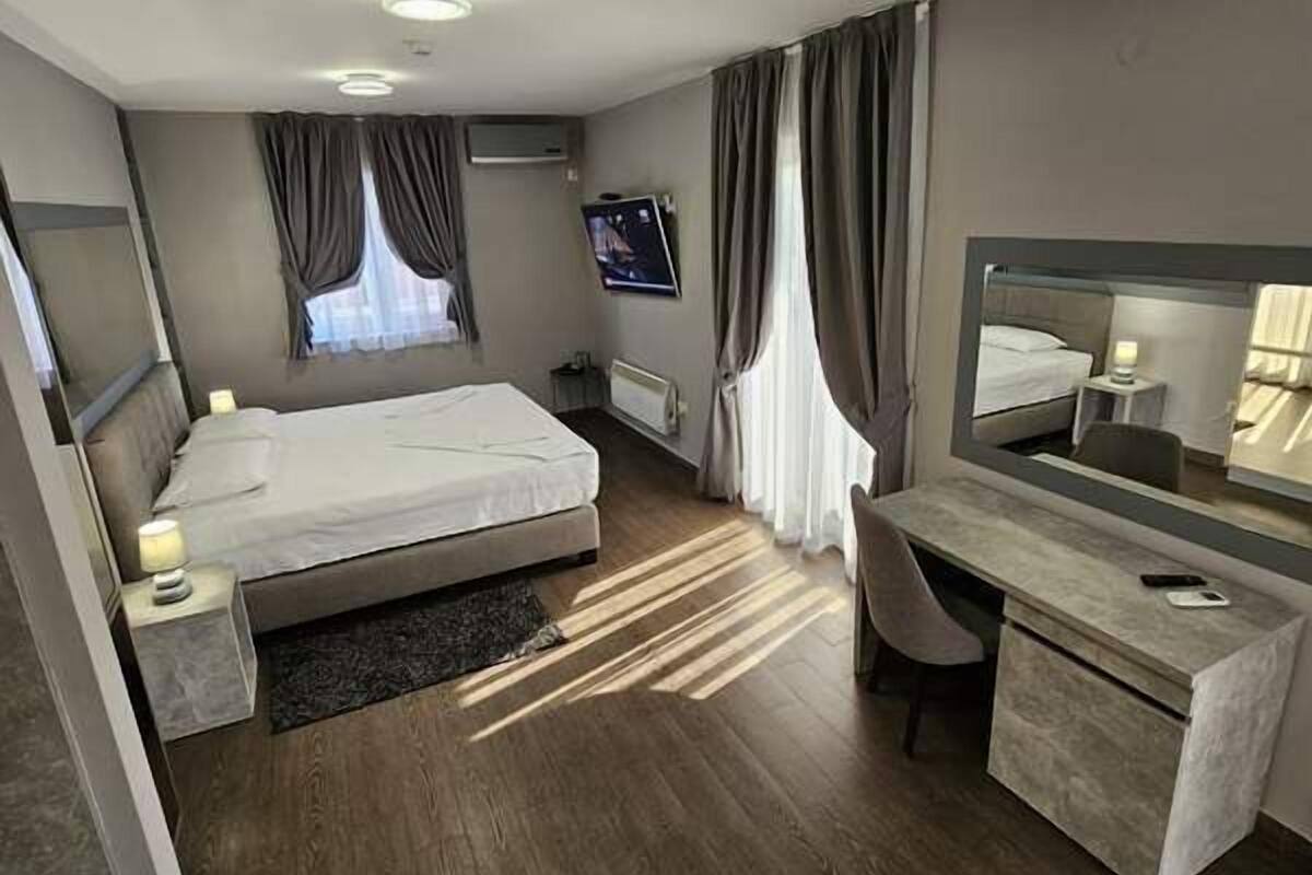 Moderni hotellihuone, jossa on sänky, työpöytä, peili ja televisio.