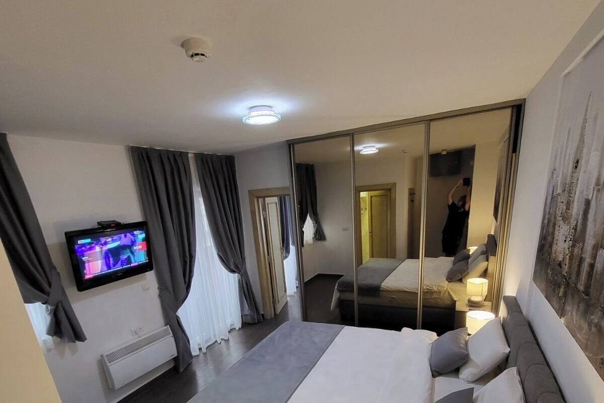 Moderni hotellihuone, jossa on suuri sänky, taulutelevisio, peili ja taulu seinällä.