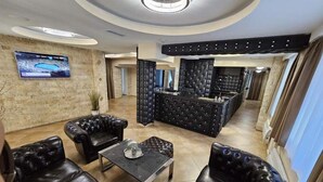 Un espace lounge moderne avec des canapés en cuir, une table basse centrale et un coin bar doté d’un dossier capitonné.