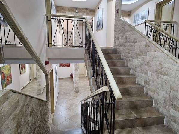 Escadaria com paredes de pedra e corrimãos pretos, levando a um andar superior.