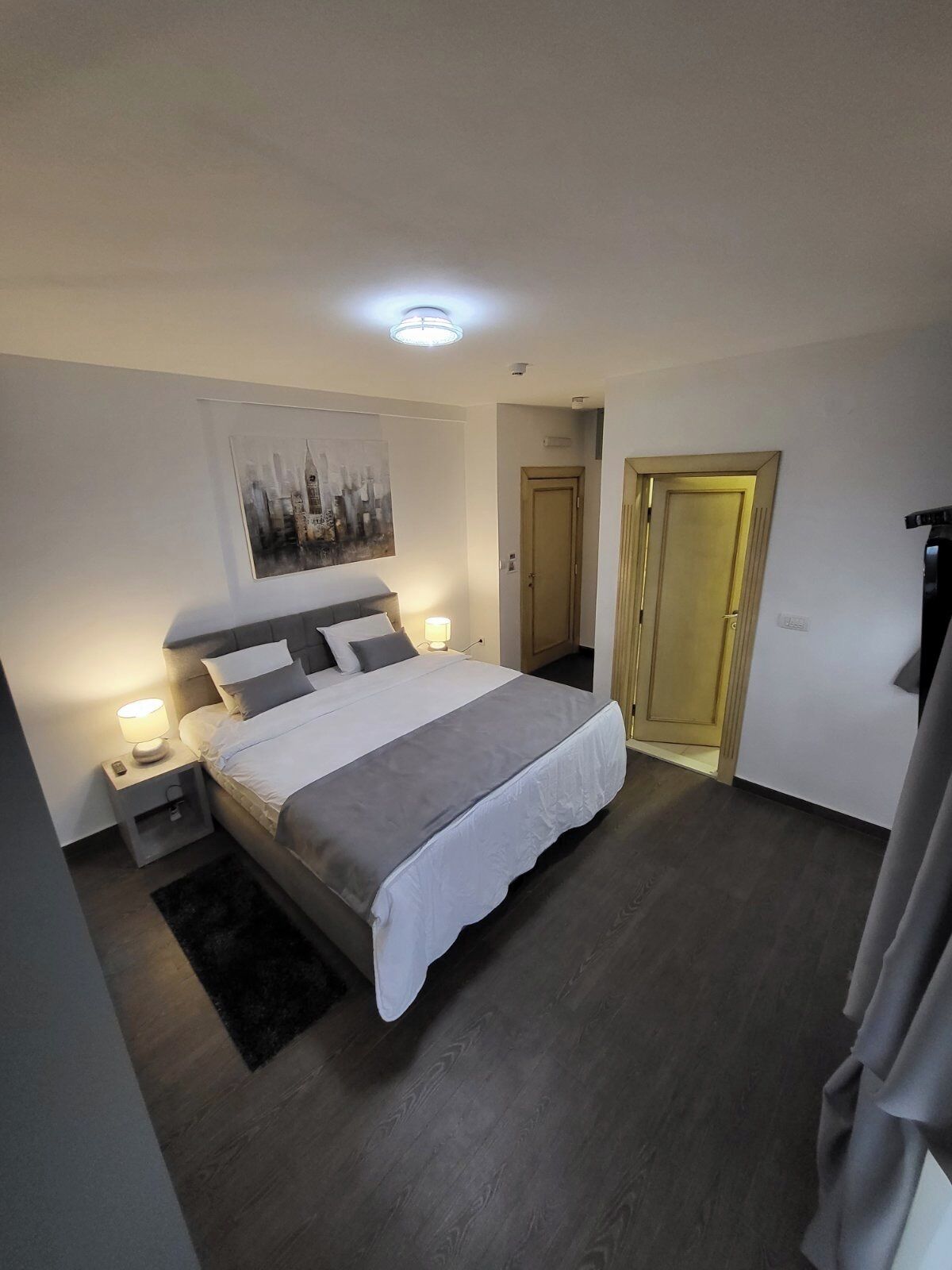Un dormitori amb un llit, làmpades de nit, una porta i un quadre a la paret.