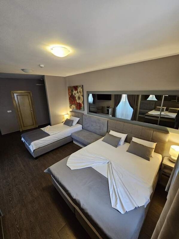 Una habitación de hotel con dos camas, un espejo grande, un cuadro y una puerta.
