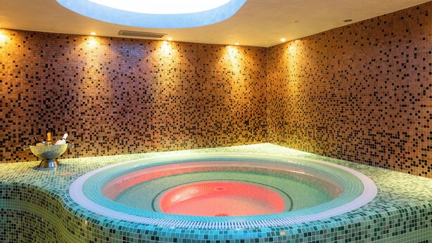 Un jacuzzi rond dont les parois sont recouvertes de mosaïques et qui est surmonté d’une verrière.