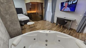 Une chambre d’hôtel moderne équipée d’une grande baignoire, d’un lit, d’un bureau et d’une télévision.