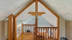 A room with a sloped ceiling, wooden beams, and a balcony with a railing.